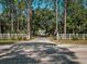 View of the property entrance featuring an electronic gate, a white fence and mature trees at 1370 Jane Lacey Ln, New Smyrna Beach, FL 32168