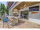 Covered outdoor kitchen features a built-in grill, bar seating, and travertine tile flooring at 1212 Commodore Dr, New Smyrna Beach, FL 32168