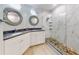 Bright bathroom with white marble walk-in shower, pebble floor, double sinks, and decorative round mirrors at 438 Bouchelle Dr # 104, New Smyrna Beach, FL 32169