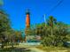 View of a brick lighthouse framed by trees, a blue building, and a road at 4752 S Atlantic Ave # 1, Ponce Inlet, FL 32127