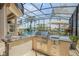 A luxurious outdoor kitchen is under a screened enclosure with a grill, bar, and view of the pool and canal at 133 Via Capri, New Smyrna Beach, FL 32169