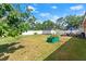 Expansive grassy backyard featuring a white fence, shed for storage, patio set with umbrella, and manicured landscape at 1851 Needle Palm Dr, Edgewater, FL 32141