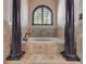 A close up on the luxury bathroom's inset tub which is framed by columns and an arched window at 610 Mura Ct, New Smyrna Beach, FL 32168