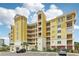 Corner view of yellow condo building with multiple balconies and parking area, surrounded by lush greenery and a clear sky at 7 Riverwalk Dr # 205, New Smyrna Beach, FL 32169