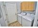 A bright laundry room features a white washer and dryer, wooden storage cabinets, and a tiled floor at 1903 Turnbull Lakes Dr # 1903, New Smyrna Beach, FL 32168