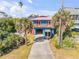 Charming blue two-story home with a wooden balcony, covered parking and a wide driveway framed by tropical palm trees at 6860 Turtlemound Rd, New Smyrna Beach, FL 32169