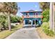 Bright blue two-story home featuring a wooden balcony, covered parking and a spacious driveway surrounded by mature palm trees at 6860 Turtlemound Rd, New Smyrna Beach, FL 32169
