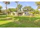 Single-story home with a green lawn, mature trees, and a bright red front door at 1144 Corbin Park Rd, New Smyrna Beach, FL 32168