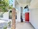 Inviting white home exterior featuring a red front door, decorative brick pillar, and manicured landscaping at 1941 Spruce Creek Lndg, Port Orange, FL 32128