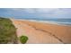 Wide shot of a sunny, sandy beach with ocean waves and vegetation in the foreground at 25 Dolphin Ave, Ormond Beach, FL 32176