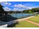 View of a community tennis court with blue surface, black fencing, and green surroundings, under a sunny, partly cloudy sky at 4403 Sea Mist Dr # 109, New Smyrna Beach, FL 32169
