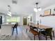 Open dining area with modern light fixture and wooden table with bench seating, flowing into the kitchen at 1421 Pine Tree Dr, Edgewater, FL 32132