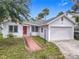 View of home with red door, lush landscaping and attached two-car garage and concrete driveway at 255 Lexington Dr, Daytona Beach, FL 32114