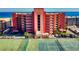 Scenic exterior view highlighting balconies, tropical trees, and a tennis court, with ocean backdrop at 4141 S Atlantic Ave # 605, New Smyrna Beach, FL 32169