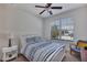 Bright bedroom with a white bed frame, bedside table with lamp, ceiling fan, and window at 9149 Outlook Rock Trl, Windermere, FL 34786