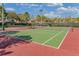 Well-maintained tennis court with green and red surface, surrounded by lush landscaping and blue sky at 4223 Arlington Ridge Blvd, Leesburg, FL 34748