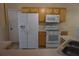 Well-equipped kitchen with white refrigerator, electric range, microwave, and wood cabinetry, offering convenient functionality at 1124 Chateau Cir, Minneola, FL 34715