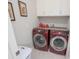 Functional laundry room equipped with modern red washer and dryer, cabinets, and white storage at 745 Asturias Rd, Davenport, FL 33837