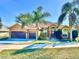 Tan one-story house with a three-car garage, palm trees, and a manicured lawn at 12941 Colonnade Cir, Clermont, FL 34711