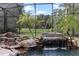 Rock waterfall spilling into the screened custom pool, surrounded by lush tropical landscaping at 3499 Rockcliff Pl, Longwood, FL 32779
