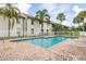 View of community pool with brick patio and white fence, surrounded by mature palm trees at 3651 N Goldenrod Rd # 204, Winter Park, FL 32792