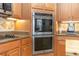 Close-up of a built-in stainless steel double oven, cooktop, and wooden cabinetry in the kitchen at 19808 Seaview St, Orlando, FL 32833