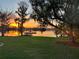 Waterfront property with lush lawn, mature trees, and boathouse, showcasing a tranquil sunset over the serene lake at 4024 W Danby Ct, Winter Springs, FL 32708