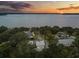 Aerial view of a lakeside home surrounded by trees and lush greenery with a beautiful sunset backdrop at 12550 Lakeshore Dr, Clermont, FL 34711