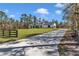 Long driveway leading to a white farmhouse with black trim and wooden columns, surrounded by trees at 8827 Sw 137Th Ct, Dunnellon, FL 34432