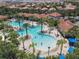 Aerial view of the pool area with palm trees, seating, and a clubhouse with a tile roof in the background at 5303 Wildwood Way, Davenport, FL 33837