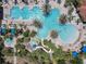 Aerial view of a large community pool area with palm trees, lounge chairs, a kiddie pool, and a water slide at 5303 Wildwood Way, Davenport, FL 33837