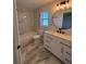 Bathroom featuring modern vanity, large round mirror, and shower over tub with white marble style tile surround at 911 Pine Ave, Mount Dora, FL 32757