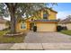 Two-story yellow house with a brick driveway and large tree at 11944 Cheltinham Dr, Orlando, FL 32824