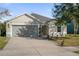 Tan one-story house with gray garage door, landscaping, and a paved driveway at 164 Pergola Pl, Ormond Beach, FL 32174