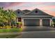 Gray house with three-car garage, palm trees, and landscaped yard at dusk at 943 Gracie Ridge St, Clermont, FL 34715