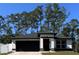 White house with black roof and garage, nestled among tall pine trees at 1490 11Th Ave, Deland, FL 32724