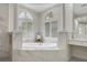 Luxurious main bathroom featuring white marble accents, soaking tub, and arched windows with plantation shutters at 408 Chelsea Ave, Davenport, FL 33837