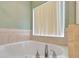 Large white bathtub with chrome faucet and tile surround under a window with blinds in the bathroom at 707 Terranova Ave, Winter Haven, FL 33884