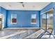 Bright bedroom showcasing blue walls, gray flooring, two windows, and sliding glass doors to the screened in patio at 10812 Woodchase Cir, Orlando, FL 32836