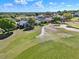 Aerial view of a community, with golf course, manicured greenery, houses, and sunny skies at 5024 St Andrews Arc, Leesburg, FL 34748
