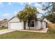 Gray house with a white garage door, landscaping, and a tree in the front yard at 5610 Great Egret Dr, Leesburg, FL 34748