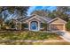 Tan one-story house with a blue front door, two-car garage, and landscaped lawn at 8835 Spyglass Loop, Clermont, FL 34711