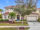 Two-story house with tile roof, landscaping, and a two-car garage. A tree is in front of the house at 6156 Broad Oak Dr, Davenport, FL 33837