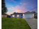 Gray house with white garage door, landscaped lawn, and a pink and purple sunset in the background at 255 Autumn Ridge Rd, Deltona, FL 32725