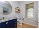 Stylish powder room with a blue vanity, gold accents, round mirror, and neutral tile floors at 2570 Marshfield Preserve Way, Kissimmee, FL 34746