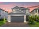 Two-story house with gray siding, gray three-car garage, and brick paver driveway at dusk at 2438 Pearl Cider Street, Orlando, FL 32824