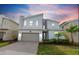 Two-story modern home with gray and white exterior, two-car garage, and landscaped lawn at dusk at 8828 Cruden Bay Ct, Davenport, FL 33896
