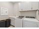 Well-lit laundry room boasts white appliances, cabinets, sink, and black laundry bins at 2496 Pine Preserve Ct, St Cloud, FL 34771