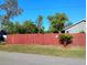Side yard featuring lush green lawn, mature shade trees, and new red wooden fence at 1886 Elkcam Blvd, Deltona, FL 32725