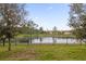 View of the fenced backyard with mature landscaping and a tranquil pond at 16737 Meadows St, Clermont, FL 34714